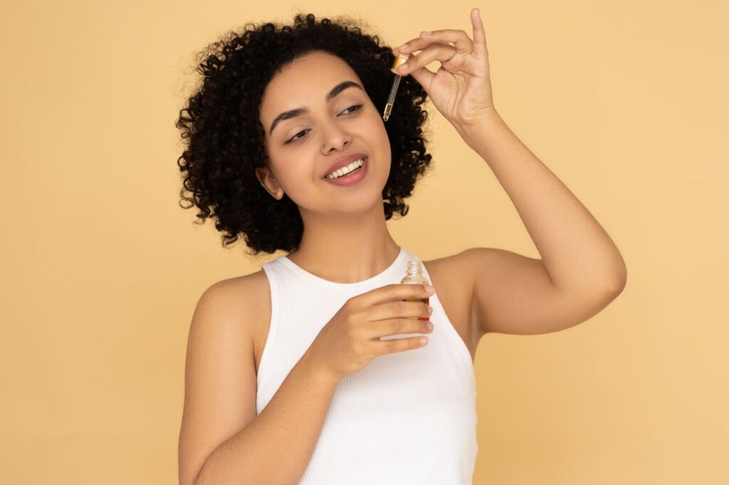 A woman with curly hair applies essential oil on her skin, promoting wellness and skincare