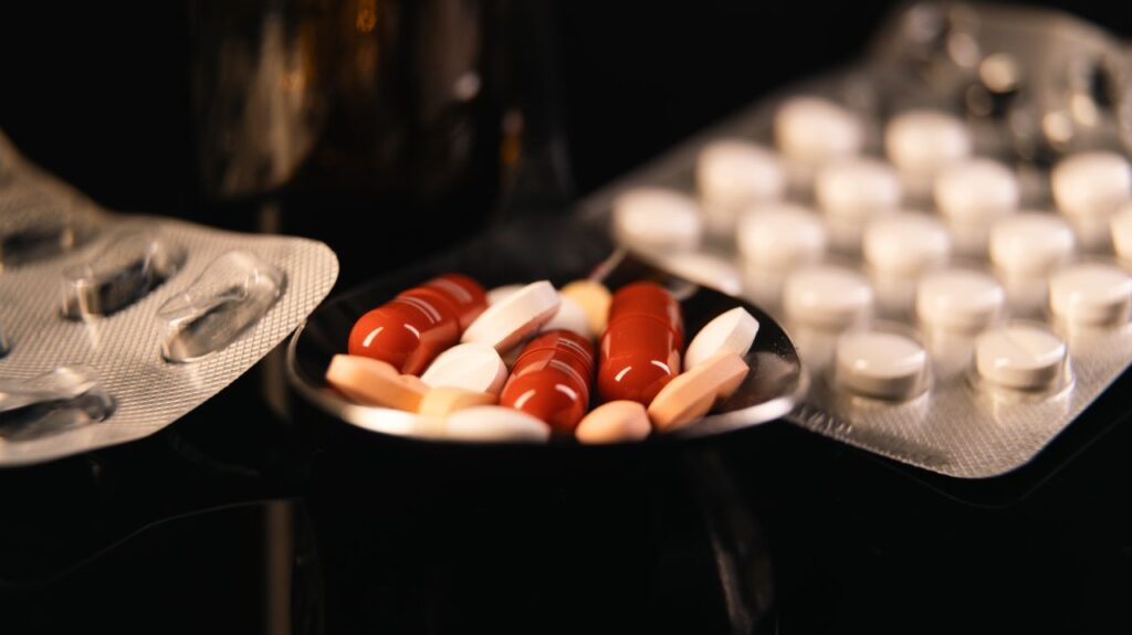 Close-up of assorted pharmaceutical pills in blister packs and a spoon on a dark background