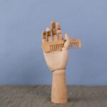 Artistic wooden hand sculpture holding a comb on a neutral backdrop. Minimalist and creative display