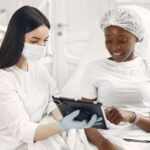 Smiling patient and dermatologist using tablet during skincare consultation