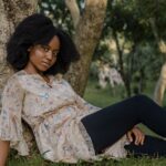 A young woman relaxes under a tree in a serene outdoor setting, capturing a moment of peace and nature