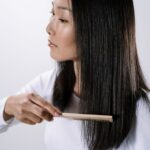 Studio portrait of an Asian woman combing her straight black hair indoors with a white background