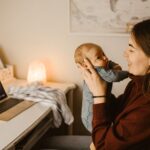 Mother holding baby while video calling from home office. Cozy and heartwarming indoor scene
