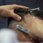 Detailed close-up of a barber using a sharp blade to shave a client's head in a salon