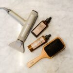 Flat lay of hairdryer, hairbrush, and styling products on a marble table
