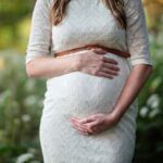 A pregnant woman in a lace dress gently cradling her belly in an outdoor setting