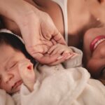A mother and her newborn holding hands, capturing a tender moment of love
