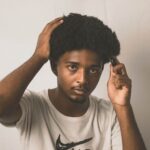 Portrait of an African American man combing his afro hair against a white background
