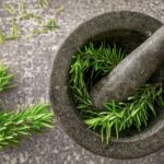Close-up of fresh rosemary sprigs in a stone mortar and pestle, highlighting natural herbs