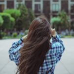 Rear view of a young woman with long hair in a checkered shirt adjusting her hair in an urban park setting