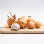 Organic onions and garlic cloves arranged on a wooden cutting board in a minimalist kitchen setting