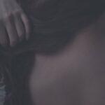 Artistic close-up of a woman gently touching her hair, capturing soft textures and intimate mood
