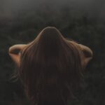Back view of a woman with long hair, standing in a misty forest