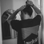 Monochrome image of a man grooming, combing hair in front of a mirror indoors