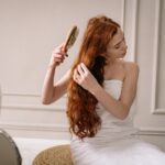 Woman with long red hair wrapped in a towel combing her hair in an elegant bathroom setting