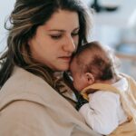 A mother gently holding her baby in a comforting embrace inside a cozy home setting