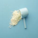 White powder spilled from a scoop on bright blue background. Clean and minimalistic food photo