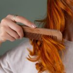 Close-up of a woman combing her red curly hair using a wooden comb against a green background