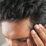 Close-up of a man's hand touching his head in contemplation. Neutral tones and soft lighting
