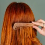Close-up of a woman's red hair being combed with a wooden comb, capturing the smooth texture